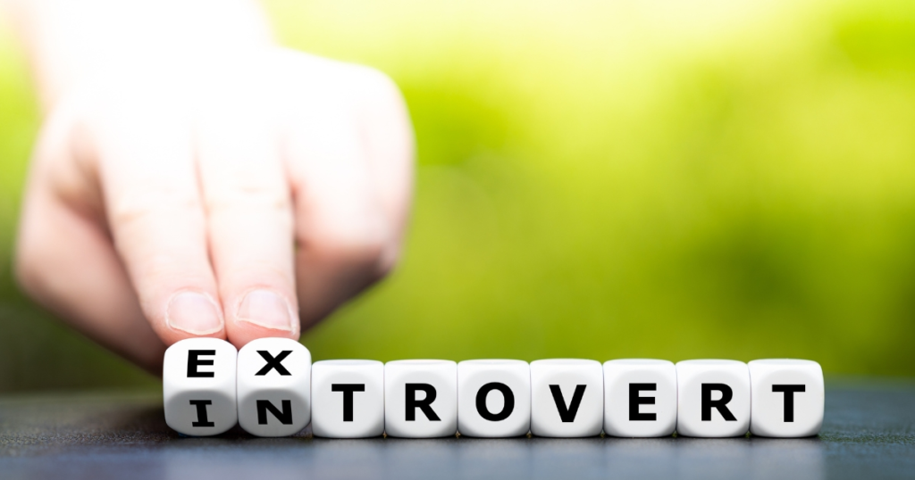 Hand arranging letter blocks to spell 'EX INTROVERT', suggesting leaving introversion.